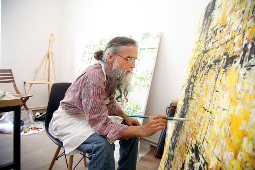 Male artist painting a modern abstract artwork in his studio. About 60 years old, Caucasian man.