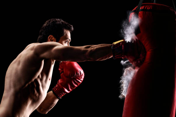 istock Strong muscular man punching a bag with boxing gloves 1318157735