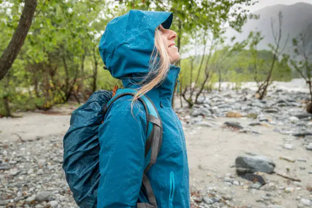 Side view of woman hiking in the rain, blue raincoat, waterproof clothing