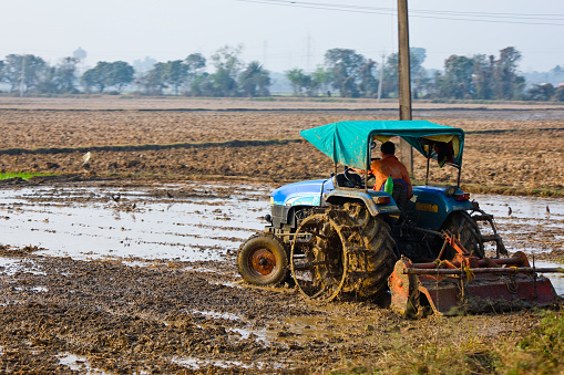 Kolkata WB India - January 25, 2021 : Taken this picture while travelling out of Kolkata using interstate. In the picture in a tractor on the farm land cultivating the land. Also the farmers sitting on the top of the load sitting on it as the vehicle is travelling slowly.