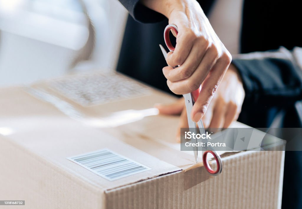 Close-up of a woman opening her courier parcel Hand of a female opening a cardboard box seal with scissor. Woman opening her courier parcel. Unboxing Stock Photo