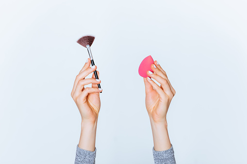 Female hands hold makeup tools powder brush and sponge on white background