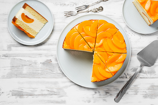Layered cheesecake with peaches on white wooden background. top view