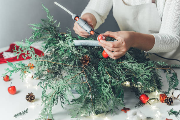 istock Florist woman makes Christmas composition for table decoration from thuja, spruce branches in wooden box. Using of floral foam, cones, snow apples, balls, cotton flowers,garland. New Year celebration 1318175381