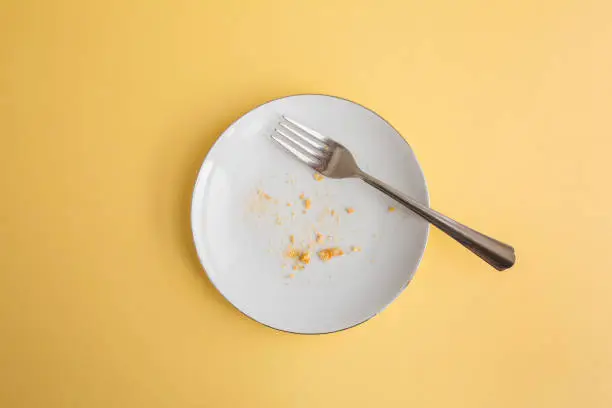 Dessert crumbs in white round plate with fork on yellow background, top view