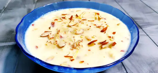 Photo of Sweet Rabdi or Lachha Rabri or basundi, made with pure milk garnished with dry fruits. Served in a bowl over moody background. Selective focus