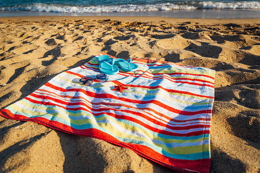 Colorful striped towel, blue flip-flops, sunglasses and red starfish on beach sand