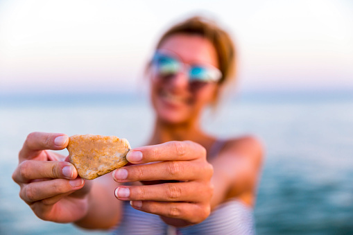 Young smiling woman holding rock on the beach