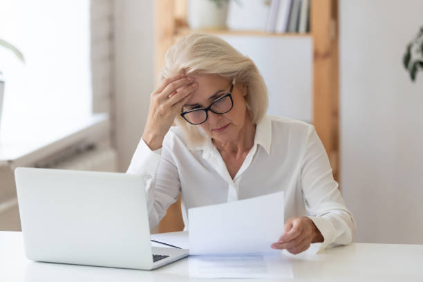 istock 60 years old serious businesswoman reading document holding ache. 1318189924
