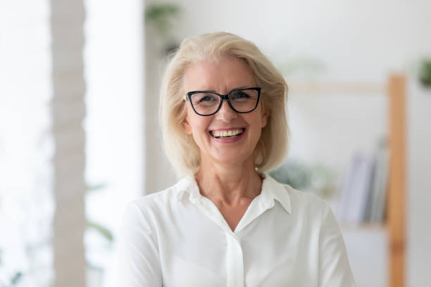 Headshot portrait of smiling senior businesswoman in office Headshot portrait of smiling senior Caucasian businesswoman in glasses pose in office on working day. Close up profile picture of happy middle-aged female employee or CEO show success at workplace. 55 59 years photos stock pictures, royalty-free photos & images