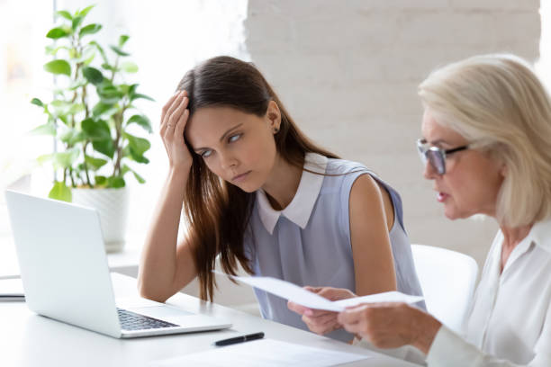 Unhappy female employee bored by colleague lecturing Unhappy young female employee bored with middle-aged colleague discuss paper document at meeting. Tired woman worker bothered annoyed by senior coworker lecture about paperwork at team briefing. business criticism stock pictures, royalty-free photos & images