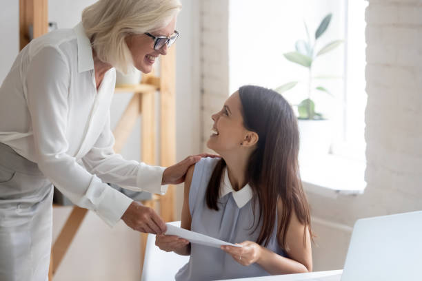 Happy businesswoman congratulate smiling female employee with promotion Smiling middle-aged businesswoman give envelope congratulate with job promotion excited young Caucasian female employee. Happy boss greeting woman worker with good work results. Reward concept. employee encouragement stock pictures, royalty-free photos & images