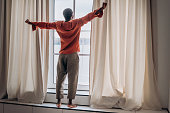 African man stretches after waking up standing at the window and looks into the distance