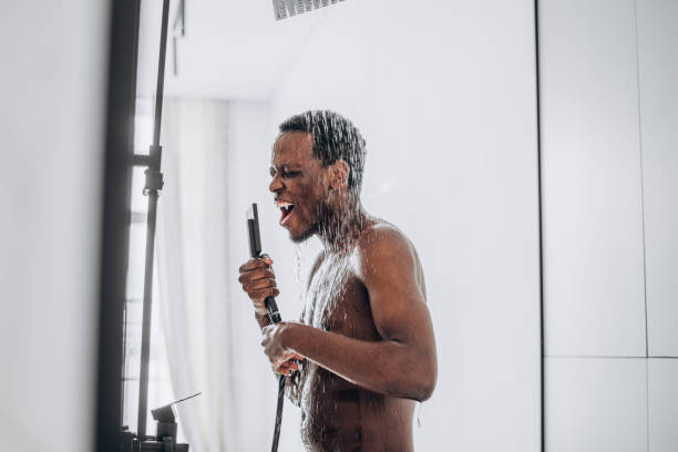 幸せなアフリカ系アメリカ人の男は、水の流れの下で想像上のマイクにシャワーで歌います - men naked shower bathroom ストックフォトと画像
