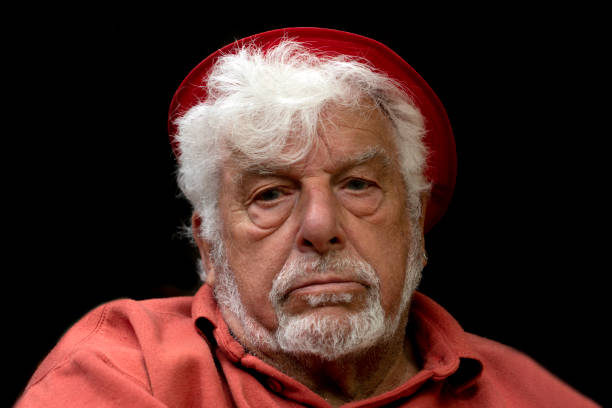Portrait of over 80 years old English man. He has a beard and he is looking at the camera. This photo was taken in doors with daylight. He was isolated with black background.