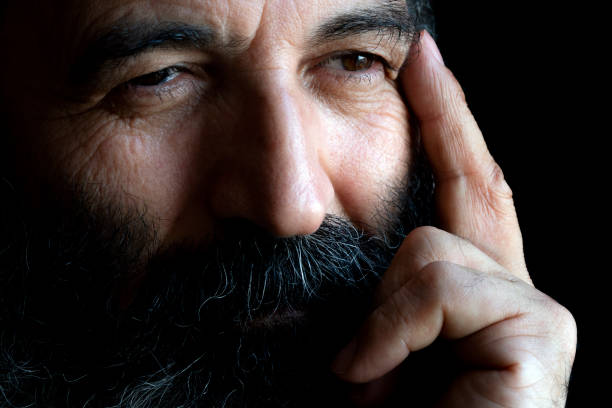 A portrait of 50-55 years old Turkish mature man. The model hand is seen in the frame. He puts his hands on his chin. This photo was taken indoors in front of the window with daylight.