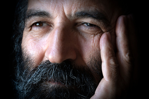 A portrait of 50-55 years old Turkish mature man.  He puts his hand on his chin. This photo was taken indoors in front of the window with daylight.