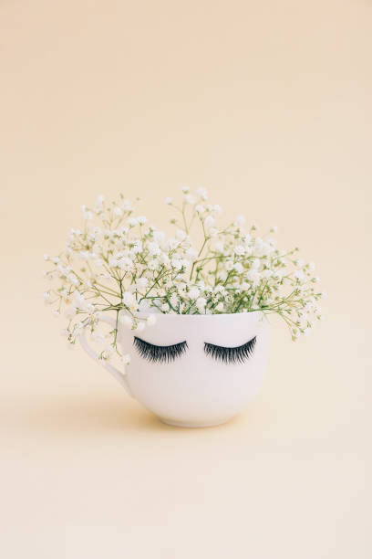 istock Creative white mug of flowers with long eyelashes on beige background. 1318202358