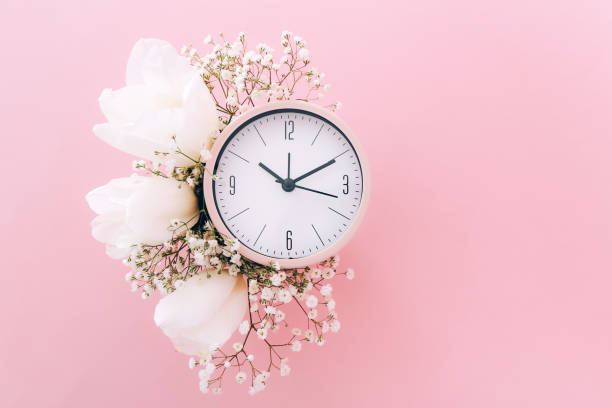 Creative minimalistic composition with a Clock. Alarm clock with flowers. Top view. On a pink background