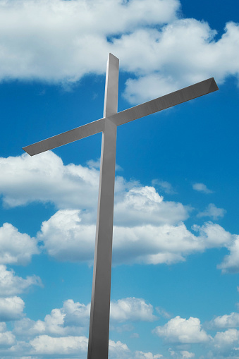 A Christian Cross for Jesus Christ on against blue sky clouds.