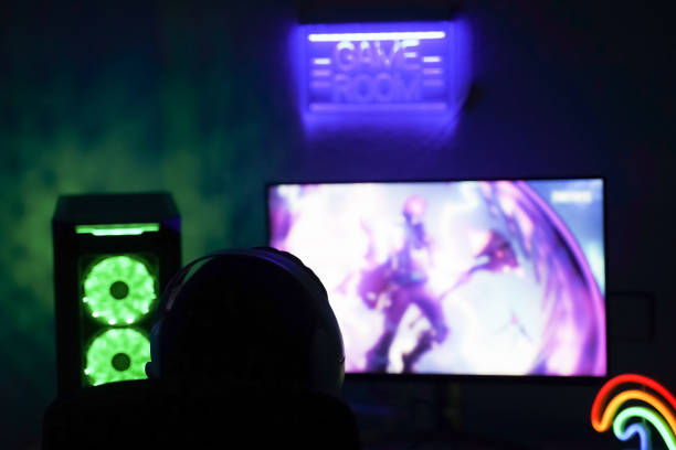 Young gamer playing video game wearing headphone. Behind view of concentrated young gamer using computer for playing game at home. Dark background and soft lights. New technology game trends and entertainment concept joven jugador jugando videojuego con auriculares. detrás de la vista del joven jugador concentrado que usa la computadora para jugar en casa. fondo oscuro y luces suaves. nuevas tendencias de juegos tecnológicos y concepto de entretenimiento