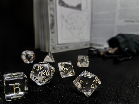 Set of transparent dice for role play, placed on a black surface, with a manual and a bag of dice in the background.