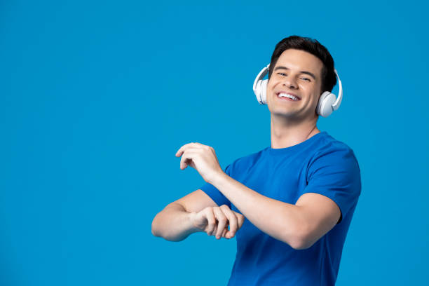 retrato de homem caucasiano feliz usando fones de ouvido ouvindo música e dançando isolado no fundo do estúdio azul - people moving audio - fotografias e filmes do acervo