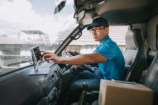 asian chinese mature male delivery person using digital tablet mobile app checking delivery information in driver's seat in delivery van