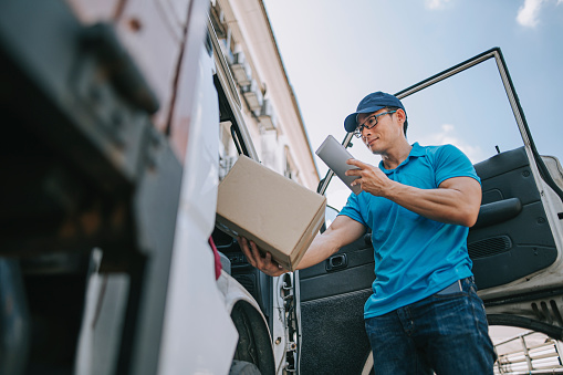 asian chinese mature male delivery person scanning barcode on package cardboard box using digital tablet