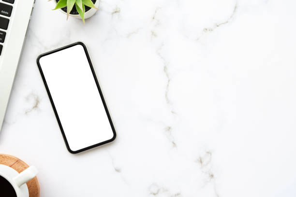 istock Smartphone with blank mock up screen is on top of white marble table with laptop computer and cup of coffee. Top view with copy space, flat lay. 1318235356