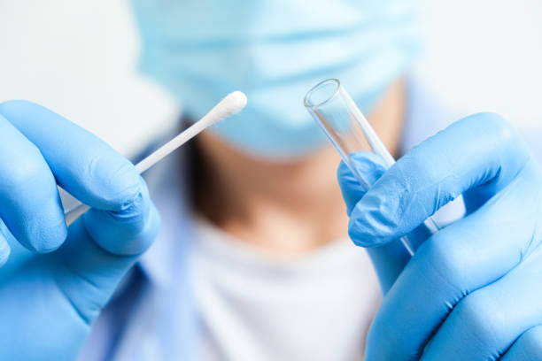 Doctor holds a COVID-19 swab collection, wears blue gloves and a PPE protective mask, and carries a test tube to collect the OP NP and  test coronavirus. stock photo