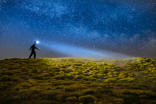 Beauty in Nature at night. Nightscape of the millions of stars in the dark blue sky over the sea and the silhouette of a person at the edge of the cliffs. Outer space and Astronomy.