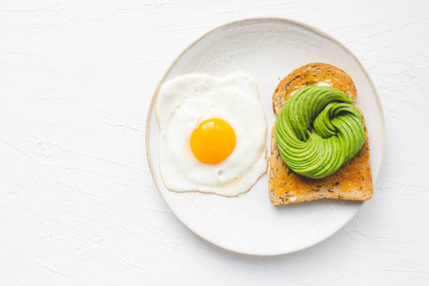 istock Sunny side up egg and avocado rosette on a toast. White plate and white background 1318242594