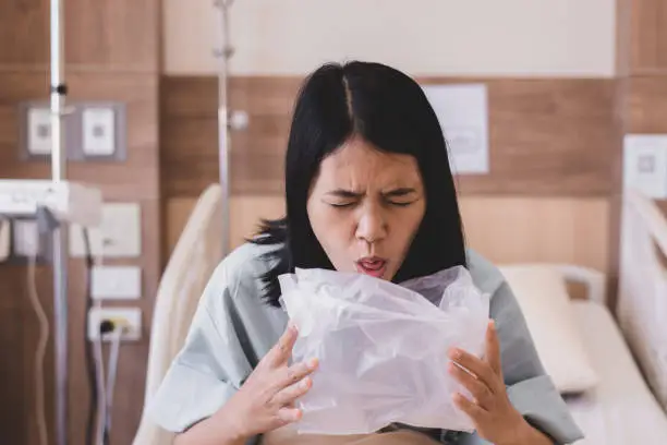 Asian woman patient puke or vomiting into plastic bag at hospital,Nausea,Indigestible