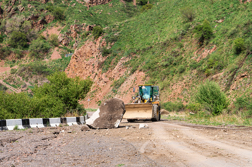 Excavator removing rocks from a mountain road after a landslide.