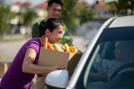 Asian female food bank volunteer received donation food at a drive through food bank.