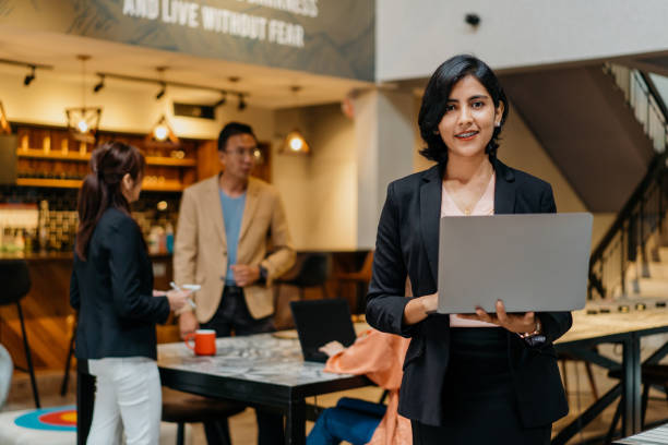 Confidence Indian businesswoman using laptop in co-working space Image of a confidence Indian businesswoman working in co-working space together with her colleagues indian ethnicity stock pictures, royalty-free photos & images