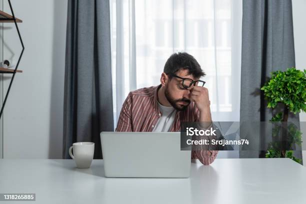 Young Freelancer Business Man Working At Home In Home Office Overworked Himself And Have Strong Headache Pain And Tired Eyes From His Laptop Screen Monitor Stock Photo - Download Image Now