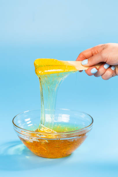 istock Yellow sugar paste for sugaring on a spatula close up on a blue background. Cosmetology and depilation concept. 1318268370
