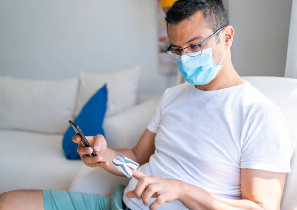 Man with protective face mask is measuring, monitoring oxygen saturation with digital pulse oximeter at home. Man with coronavirus, covid-19 pandemia quarantine lockdown.  Digital Pulse Oximeter at Home to Test Oxygen Level in Blood And Pulse Rate. Man with protective face mask is measuring, monitoring oxygen saturation with digital pulse oximeter at home. Man with coronavirus, covid-19 pandemia quarantine lockdown.  Digital Pulse Oximeter at Home to Test Oxygen Level in Blood And Pulse Rate. oxygen monitor stock pictures, royalty-free photos & images