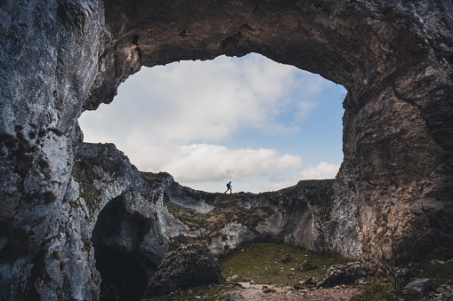 Panoramic view of cave mouth with a hiker standing in front of cave. Portupekoleze arch, Navarre, Spain.