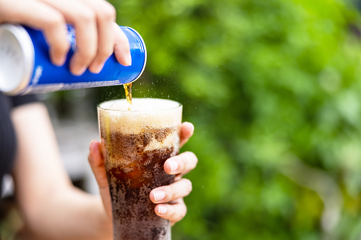 Female hand pouring cola drink from tin to glass