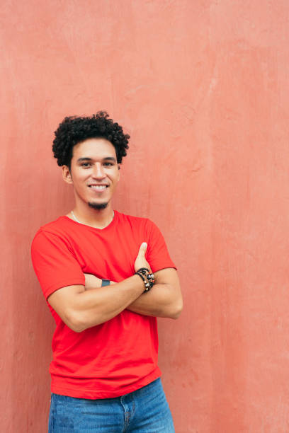 istock Handsome young Hispanic man with his arms crossed while standing against red wall 1318277125