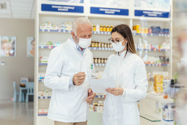 istock Colleague advice. Documentation and paper work in pharmacies during corona virus. A senior pharmacist explains the documentation in the pharmacy to a young pharmacist They wear uniforms and face masks 1318289185