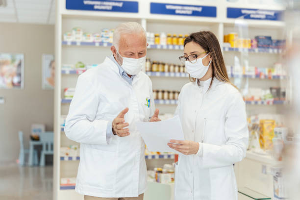 istock Colleague advice. Documentation and paper work in pharmacies during corona virus. A senior pharmacist explains the documentation in the pharmacy to a young pharmacist They wear uniforms and face masks 1318289218