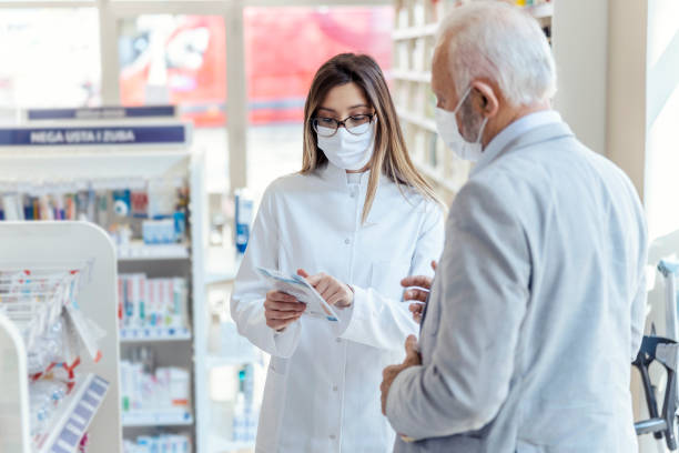istock Help from a pharmacist. A female pharmacist with glasses holds medicine boxes and instructions for use. She looks at the man who is explaining something else. They both wear protective masks 1318290369