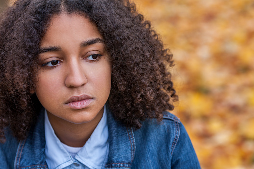 Beautiful mixed race African American girl teenager female young woman outside looking sad depressed or thoughtful, mental health concept