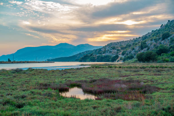Beautiful summer landscape with lake and mountains at sunset. Green grass and clouds on the sky.