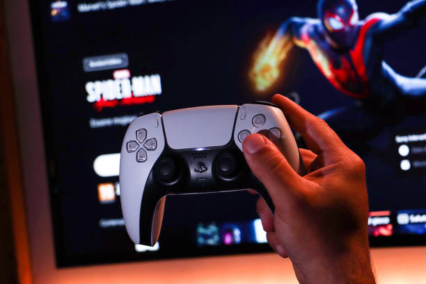 Controller DualSense Sony Playstation 5 Ancona, Italy - May 16, 2021: Sony Playstation 5 DualSense Controller with Player Hand. In the background you can see the Playstation Plus Store screen with the Marvel's Spider-Man Miles Morales Standard Edition video game. brand name games console stock pictures, royalty-free photos & images