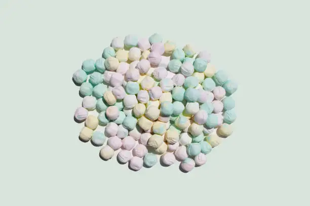 Photo of after dinner mints in pink yellow and green colors in a heap pile on a light off white studio space as food scene